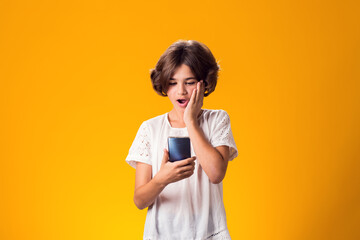 Surprised kid girl holding smartphone in hand over yellow background