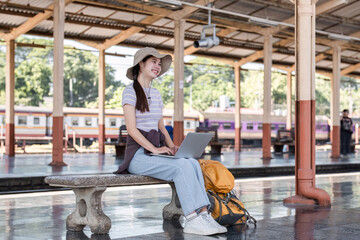 Young Asian woman in modern train station Female backpacker passenger sitting on a bench using a...