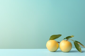  a couple of yellow apples sitting on top of a table next to a green leafy branch on a light blue background.