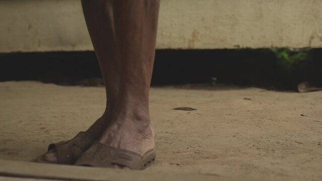 The legs of an elderly Asian man in sandals are standing and walking beside him.