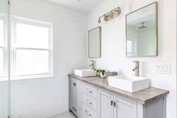An elegant, renovated bathroom with white sinks, grey vanity, granite countertop, and bronze hardware, faucets and light.