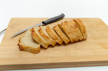 Slices of fresh bread and a cutting knife on a wooden board. White background, isolated.