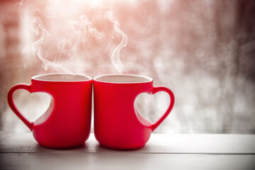 two heart shaped mugs with tea on the background of a window in winter
