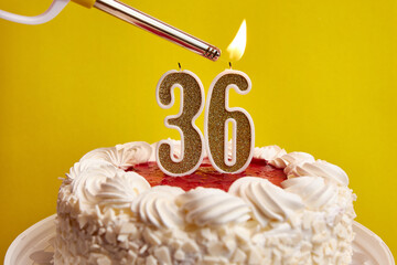 A candle in the form of the number 36, stuck in a festive cake, is lit. Celebrating a birthday or a...