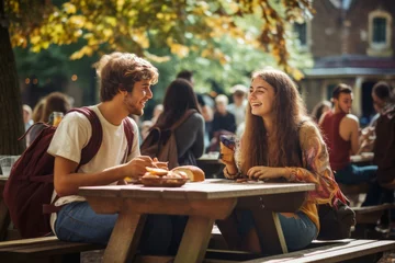 Fotobehang Two students boy and girl have lunch on campus or college on a warm summer day. Friends or couple are sitting on wooden benches at the table talking and eating. Generated by AI. © Nikolai