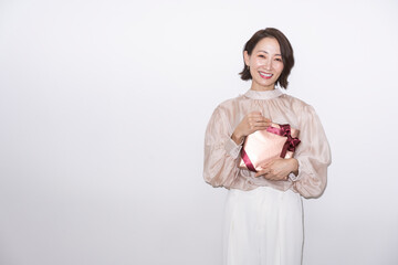 プレゼントの箱を持ち微笑んでいるミドル世代の女性/スタジオ撮影白背景