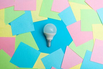A small white LED lamp in the middle of colorful pieces of paper on a blue background. The concept...