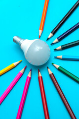 A white LED lamp surrounded by colored pencils on a blue background. The concept of one idea with a difference of opinion.
