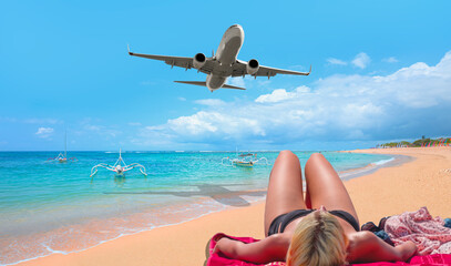 Fototapeta na wymiar Back view of woman in bikini relaxing at sand beach, Bali - Airplane flying over tropical sea at sunset