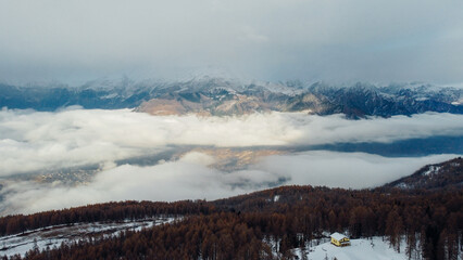 Naklejka premium Aerial view of winter landscape with mountain peaks covered with snow, fluffy clouds and coniferous forest. Natural background.