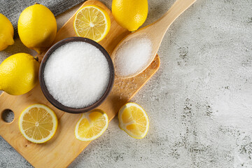 Citric or lemon acid in clay bowl with a spoon, close-up, and whole ripe lemons on gray background....