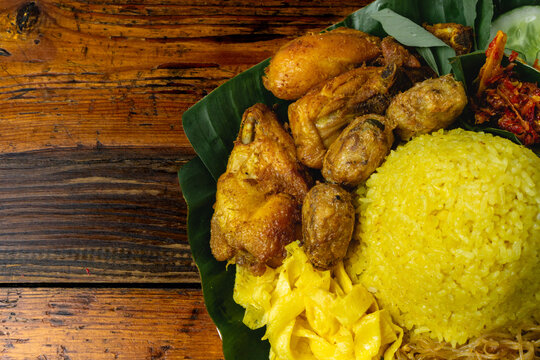 nasi kuning or nasi tumpeng, steam rice with turmeric, fried chicken, tempeh, sambal and fresh vegetables on top of banana leaves