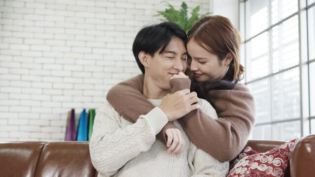 Happy asian young girlfriend embracing from back boyfriend in feeling love while sitting in sofa, care and support. Home bond, special event or marriage love