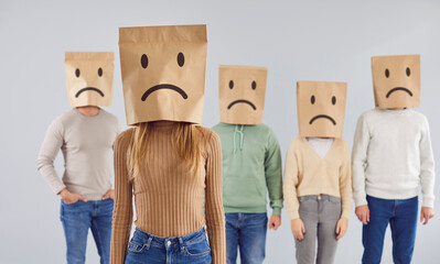 Diverse group of individuals wearing paper bags with drawn sad faces on heads, creating a unique...