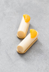 Two Tangerine cream cakes of cylindrical shape, dessert bars. On cookies. Decorated with a slice of tangerine. Light gray background. Close up