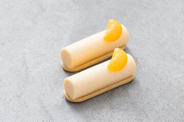 Vegan dessert. Two Tangerine cream cakes of cylindrical shape, dessert bars. On cookies. Decorated with a slice of tangerine. Light gray background. Close up