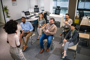 Fototapeta premium Young business woman lecturing her multiethnic colleagues. Having a speech while holding a microphone.