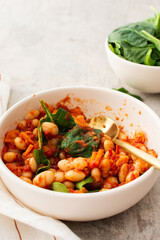 Healthy breakfasts and lunches, stewed white beans with carrots, onions and tomatoes with spinach leaves, a bowl of beans and spinach