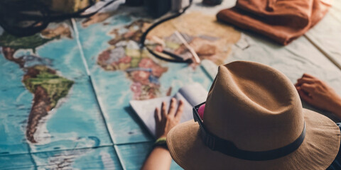 Fototapeta na wymiar A person wearing a hat planning a holiday. Looking at a map and writing in a book. Vacation preparation. Wanderlust