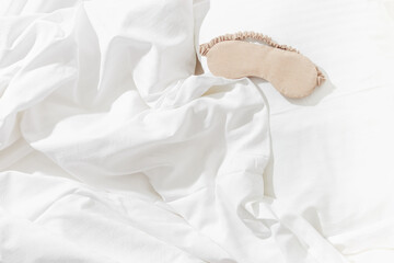 Fototapeta na wymiar Beige eye mask for sleep on white bedclothes at home, minimal lifestyle aesthetic flat lay photo. Top view Female sleeping mask for best sleepers, for travel, comfort relaxation. Rest well concept.