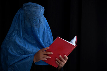 Afghan Muslim woman with burka tradition cloths in Afghanistan and West Pakistan, studying holy Quran against the dark background, with copy space