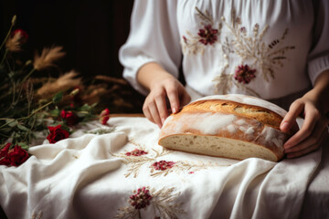 Hands present a loaf of bread on an embroidered cloth. The concept of traditional baking and heritage.