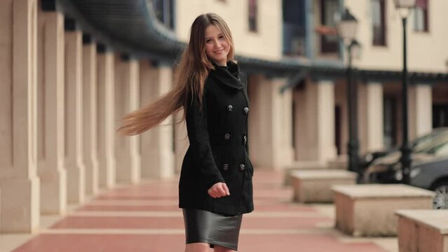 Slow motion. A strong, confident woman turns around and smiles at the camera, long hair fluttering in the wind. Dynamics and expression. Business woman, student on a walk in the city. Motion, movement