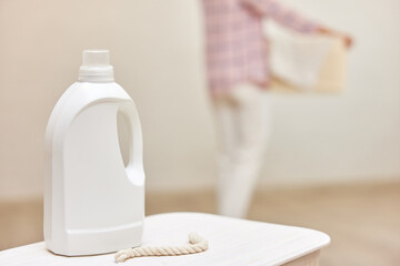 washing gel or fabric softener on white laundry basket against the background of blurred woman with basket of laundry . Mock up, copy space.