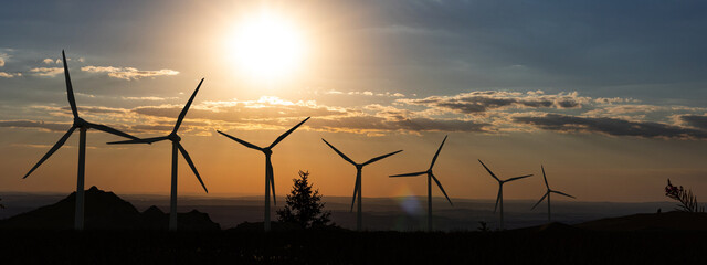 Silhouette of wind turbines in a row. Sky with clouds during sunset. Renewable and sustainable...