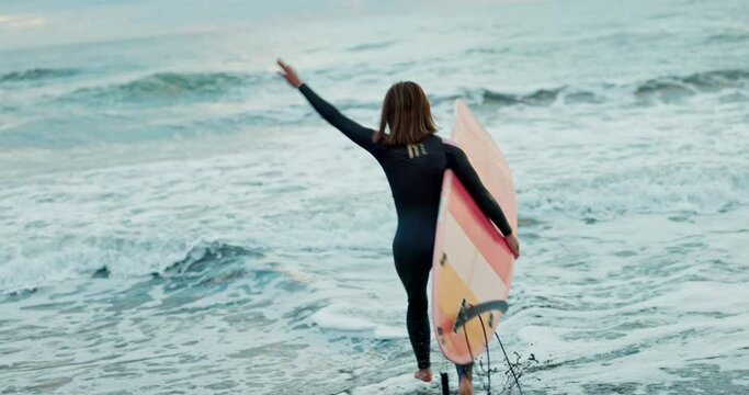 Back, woman and running into ocean with surfboard at beach, ready for fitness in wet suit, sports and surfing in nature. Energy, action and waves with surfer, professional or hobby for extreme sport