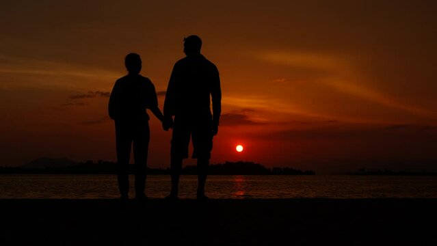 Lovely couple against colorful river evening. A lovely couple silhouette stand on river beach and enjoy the calm sunset in summer.