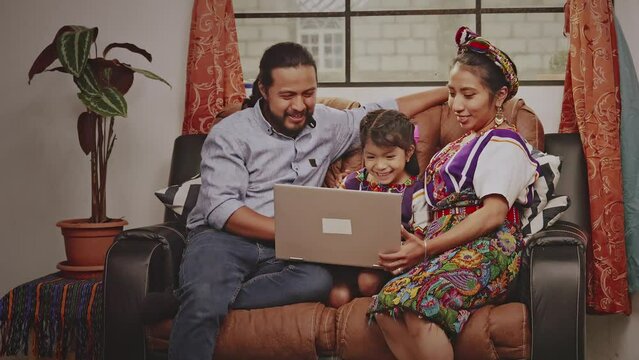 Hispanic family on the sofa in their living room .
Mayan indigenous family in a rural area use technology to educate their little girl.