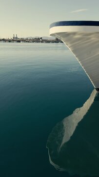 A moored ship rocks on the waves. Reflection in the water of the port at the pier. Ropes hold the white ship at the pier. Spain. Grao, Castellon