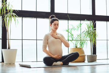 Meditation during pregnancy. Young calm tranquil pregnant woman doing yoga at home, meditating and...