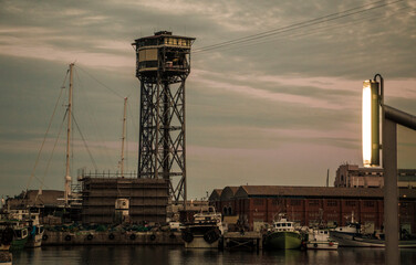 An industrial port scene with a big steel tower and fishing boats