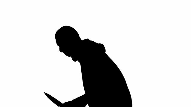 Black silhouette of thief on isolated white background. A male robber in a hoodie and balaclava walks with a knife in his hands, preparing to commit a crime. Side view.