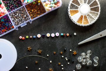 Colorful beads and various jewelry making supplies on dark background. Letter beads spelling I...