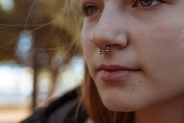 Young woman with a nose piercing against a blurred street background, close-up.