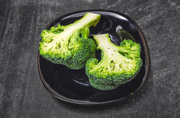 Two halves of fresh green broccoli in a black bowl on a gray background. A healthy diet.