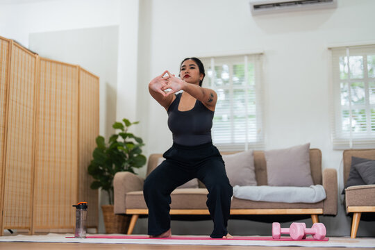 Overweight woman enjoying a fitness workout at home. Fat, plump woman and squatting on an exercise mat in the living room