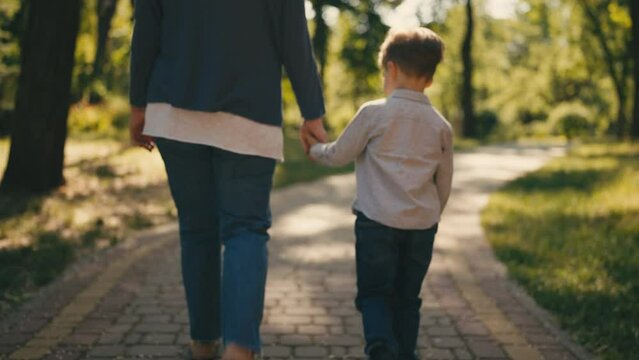 Grandmother and little grandson holding hands, walking together in sunny park