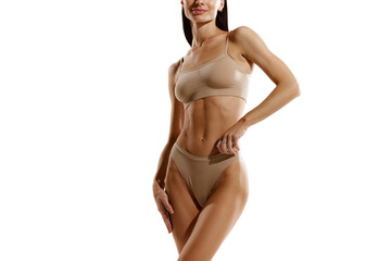 Cropped image of young woman with slim body shape standing in beige cotton underwear against white...