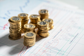 Stack of pound coins on financial graphs and figures