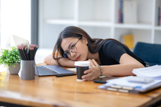 Freelance Asian businessperson, A businesswoman sits slumped on arm at her desk in a bored mood. Distracted while taking a break from  busy schedule.