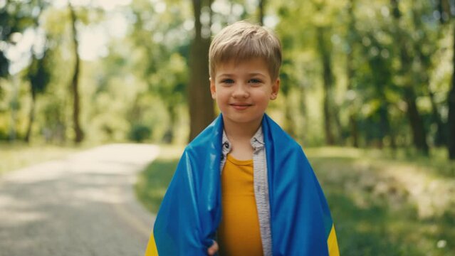 Cute little boy smiling wrapped in Ukrainian flag in summer park, nations future