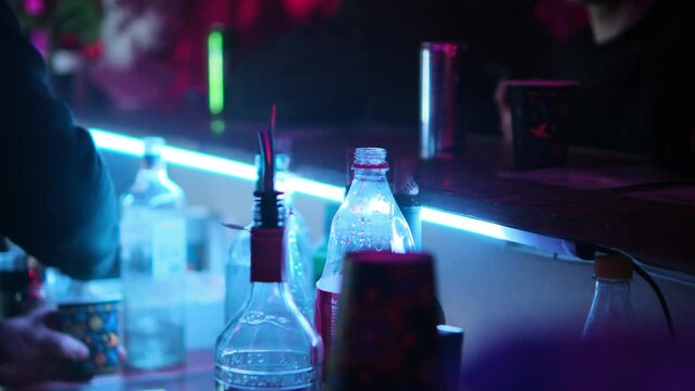 The bartender pours an alcoholic beverage into a paper glass and places it on the bar counter. Selective focus.