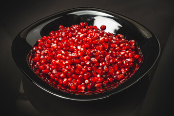 Ripe red pomegranate seeds in a black bowl. Dark background. Useful fruits for health.