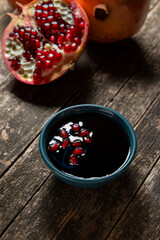 Pomegranate molasses in small bowl on rustic wooden table. Pomegranate sweet and sour syrup with pomegranate fruits behind.