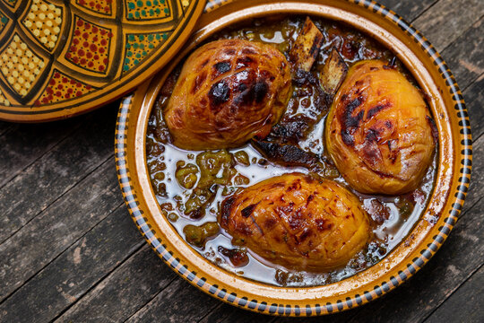 Moroccan lamb and quice tagine dish in open traditional tagine pot on rustic wooden table.