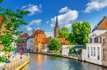 Sint Annarei water canal of Reie river, old buildings on embankment in Brugge old town, Bruges city historical centre, Saint Anna Church tower spire, West Flanders province, Flemish Region, Belgium - obrazy, fototapety, plakaty